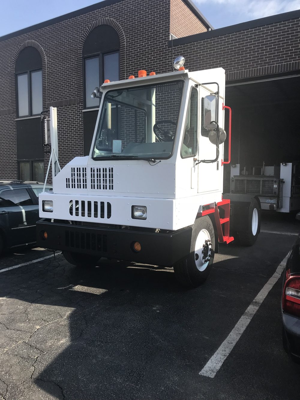 A white yard tractor with red steps in the lot of the brick office with arched windows