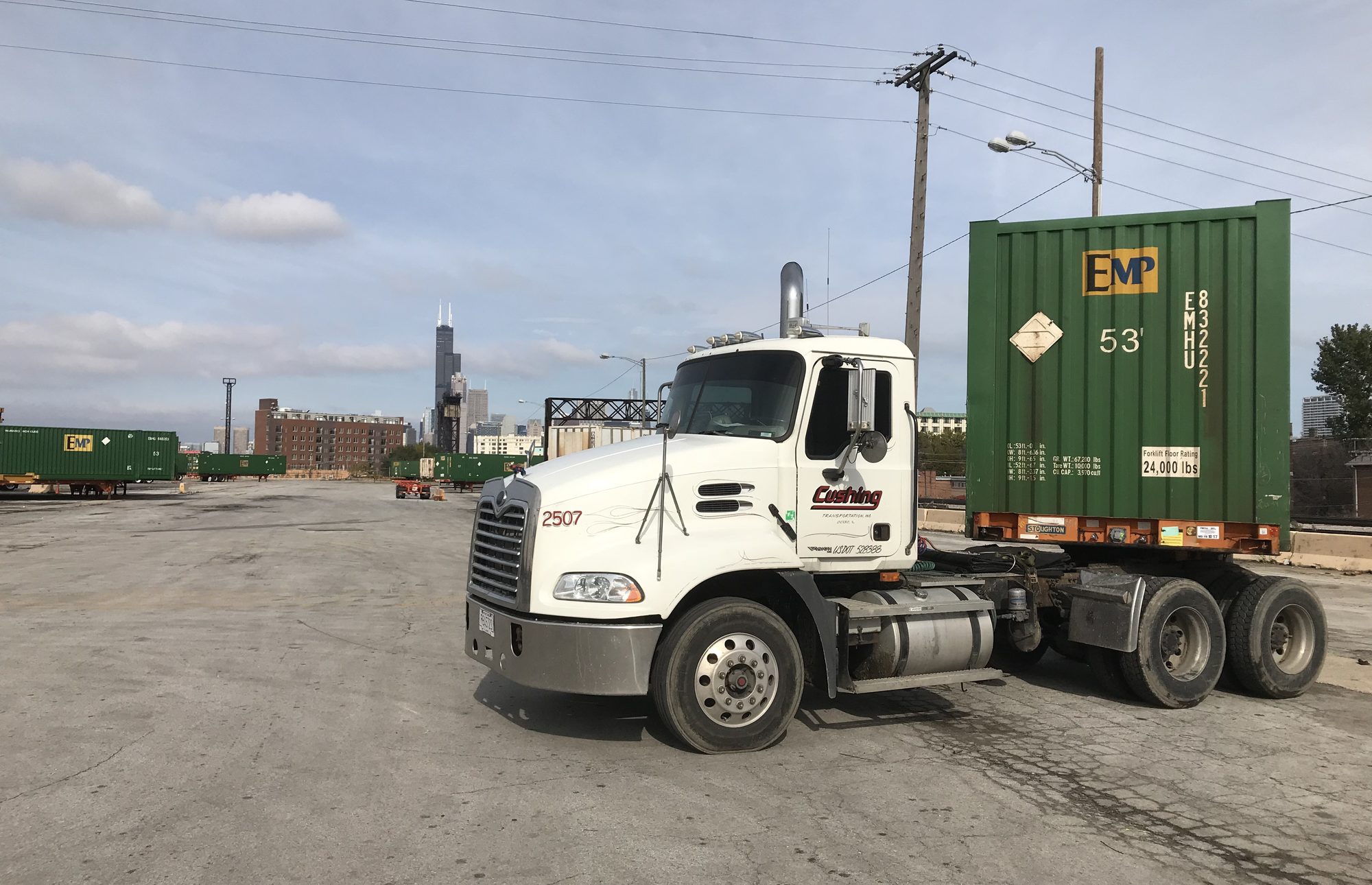 Cushing tractor 2507 under a 53-foot EMP container on a chassis at a Chicago rail ramp, the Willis Tower on the skyline behind