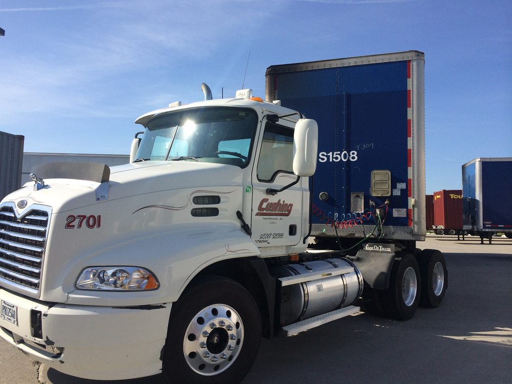 Cushing day cab 2701, a white Mack with Cushing Transportation lettering on the door, coupled to a blue trailer in a trailer yard under a blue sky